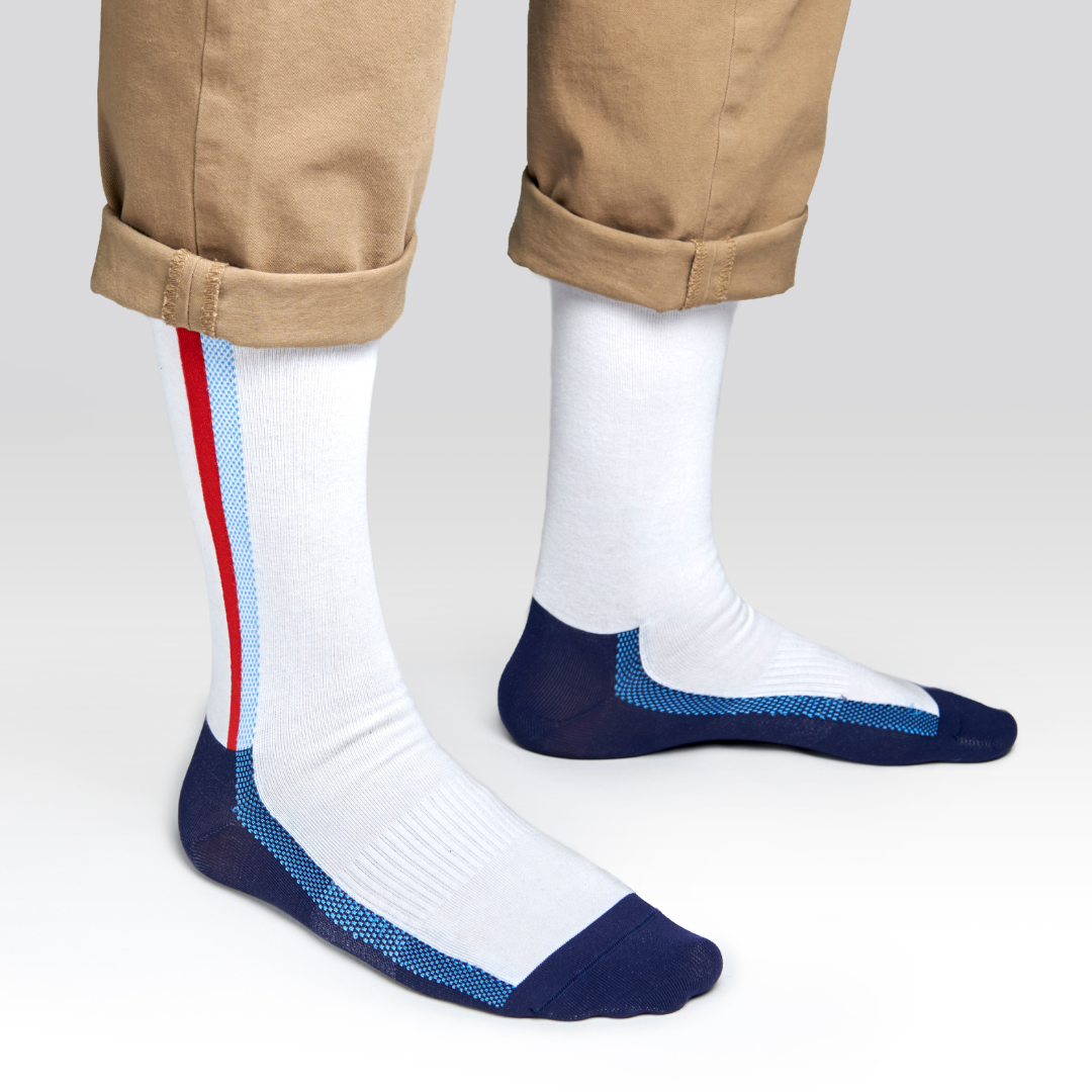 A person wearing tan pants with cuffs, showing white crew socks featuring blue toes, heels, and side stripes, plus a single red stripe on the outer sides.