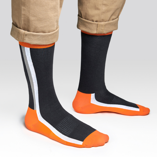 A person wearing dark socks with orange toes, heels, and cuffs, plus a white and orange diagonal stripe design. The person’s pants are khaki and rolled up at the cuffs.