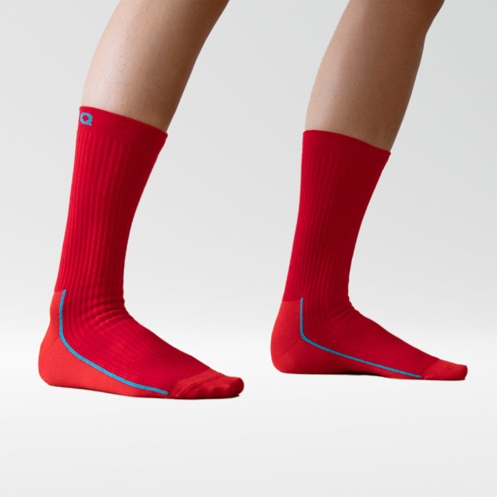 A pair of legs wearing bright red, calf-length socks with blue trim on a plain white background. The feet are slightly apart, and only the lower legs are visible.