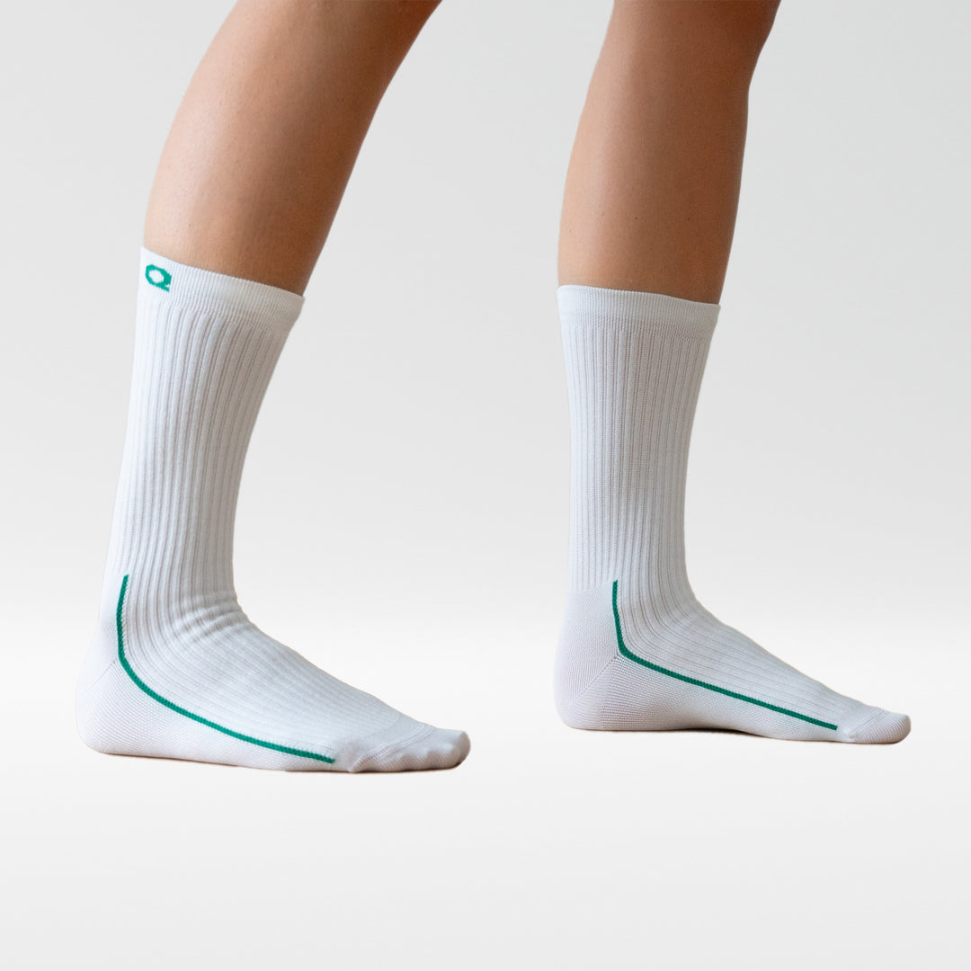 A person wearing white calf-length socks with green accents stands on tiptoes against a plain white background.