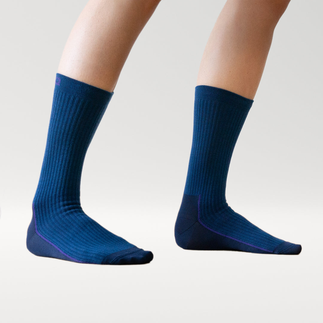A pair of feet wearing ribbed, dark blue socks with purple accents, shown against a plain light background. The socks are mid-calf length and fitted.