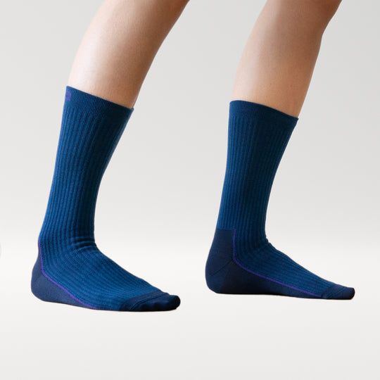 A pair of feet wearing ribbed, dark blue socks with purple accents, shown against a plain light background. The socks are mid-calf length and fitted.