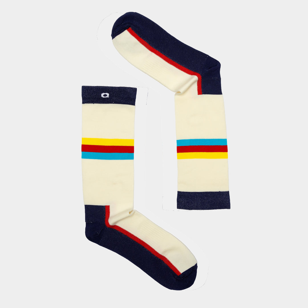 Two cream-colored socks with navy toes, heels, and cuffs, featuring horizontal red, yellow, and blue stripes across the middle, are arranged on a light background to form the number 1.