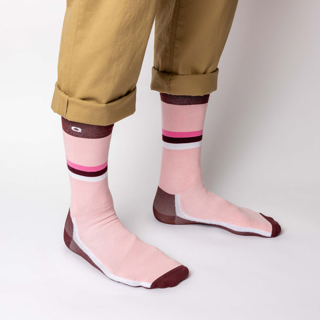 Person wearing tan cuffed pants and pink crew socks with maroon toes, heels, and top bands. The socks also have white and maroon stripes around the ankles, and the person is standing on a white background.
