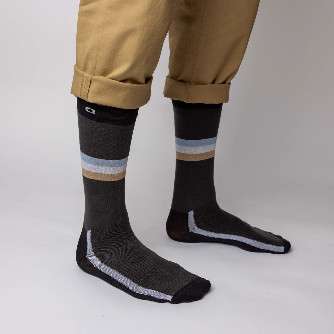 Person wearing tan pants rolled up at the cuffs, showing dark socks with light blue, tan, and white stripes around the calves, standing on a neutral background.