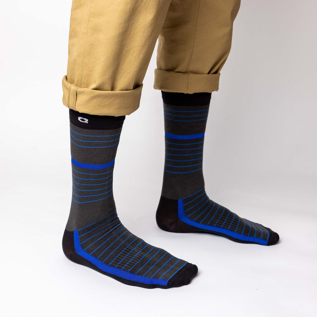 Person wearing tan pants with cuffs rolled up, showing dark gray socks featuring blue and light gray horizontal stripes, standing on a white background.