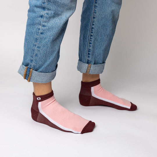 A person wearing rolled-up blue jeans and pink ankle socks with burgundy toes, heels, and cuffs stands against a plain white background.