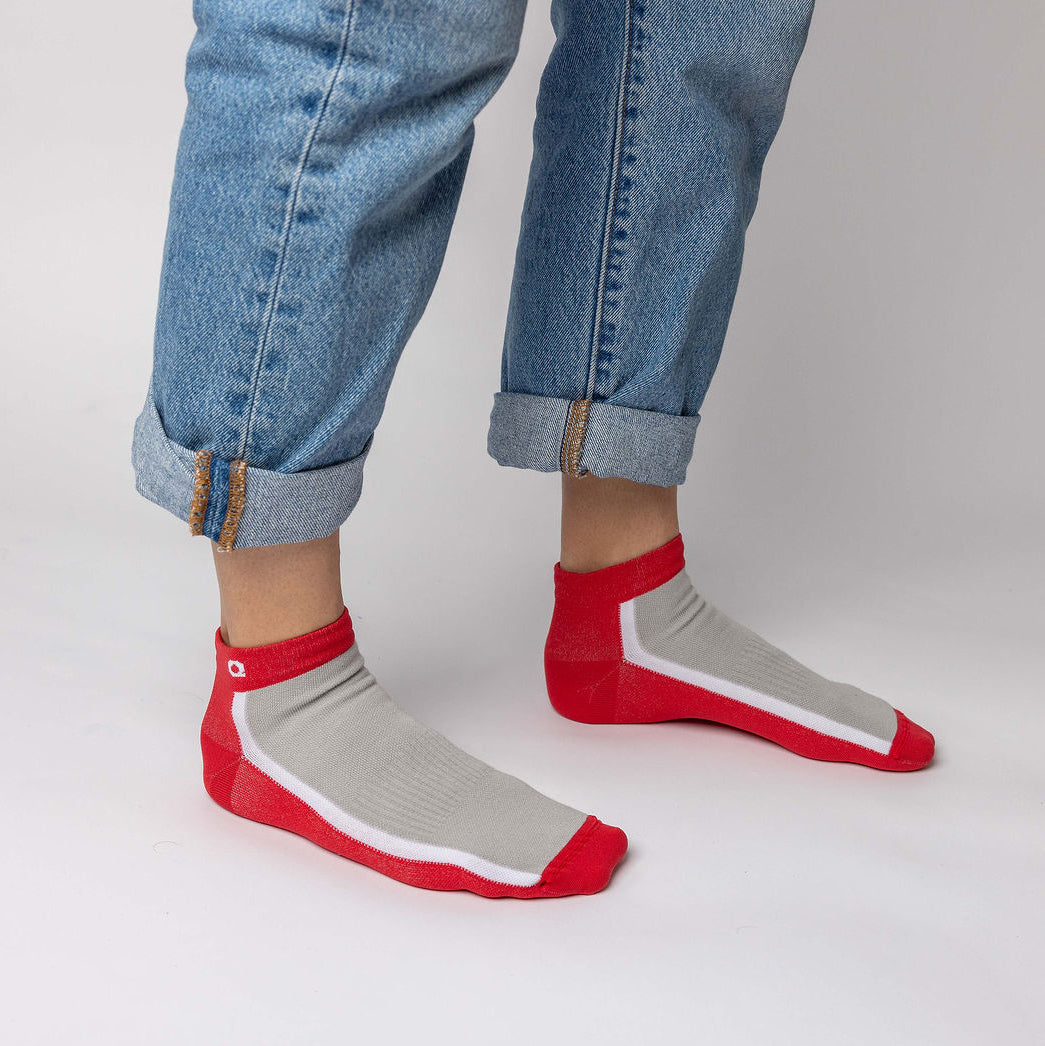 A person wearing rolled-up blue jeans and gray ankle socks with red toes, heels, and cuffs, standing on a plain white surface.