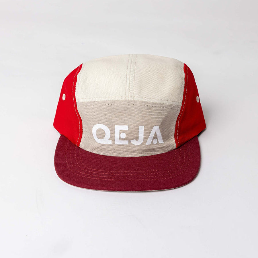 A five-panel cap with a beige front and top, red sides, and a burgundy brim. The front panel features the bold, white letters QEJA.