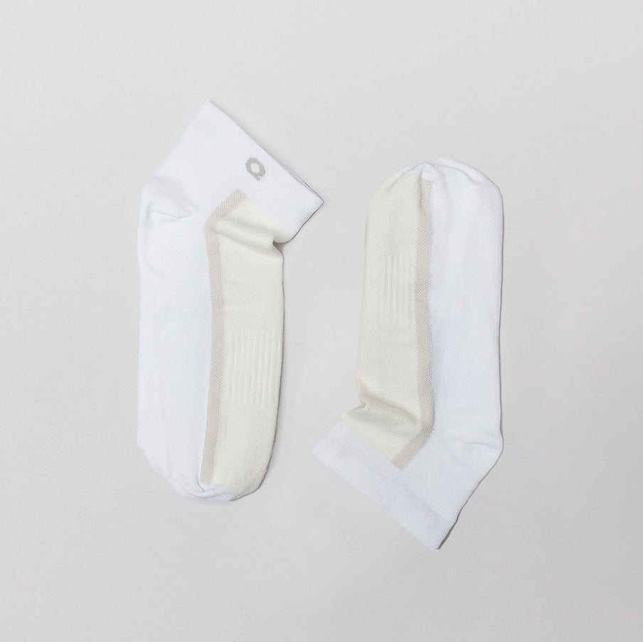 Two white ankle socks with light beige details are laid flat on a light gray background, positioned side by side with the toes pointing in opposite directions.