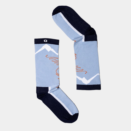 A pair of light blue socks with dark blue toes, heels, and cuffs, featuring white mountain designs and orange squiggles, laid out on a light background to form the letter Q.