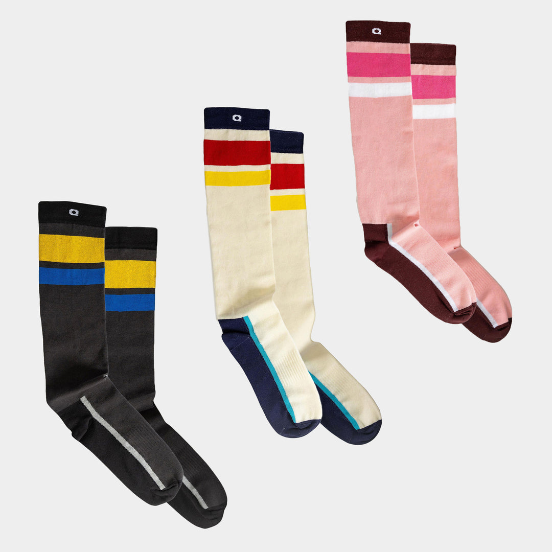 Three pairs of knee-high socks with colorful stripes: one black and yellow with blue stripe, one cream with red, yellow, and blue stripes, and one pink and brown with white and fuchsia stripes, all on a white background.