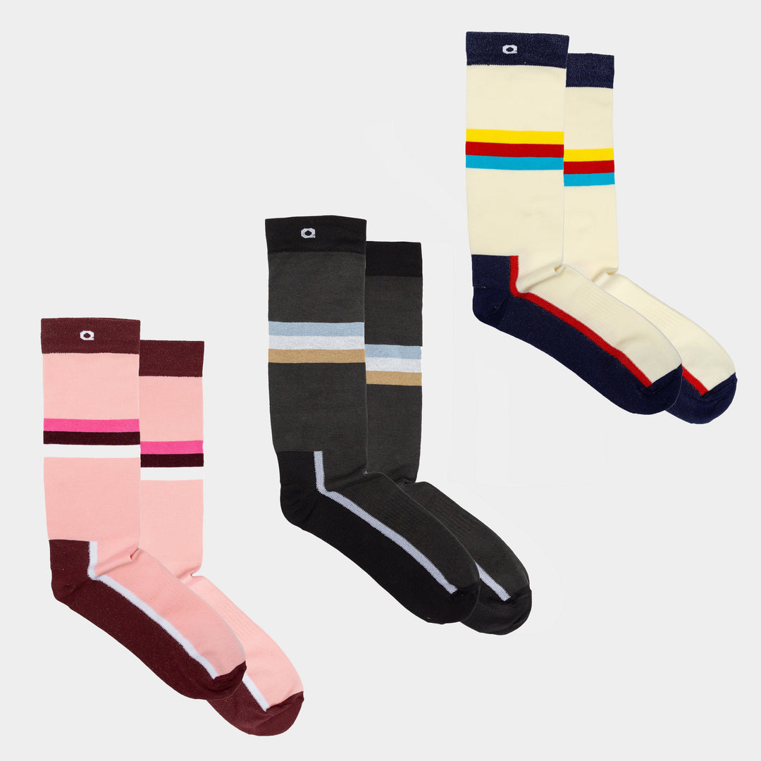 Three pairs of knee-high socks in different colors: pink and maroon with stripes, black and gray with stripes, and cream with blue and red stripes, all laid out on a plain white background.