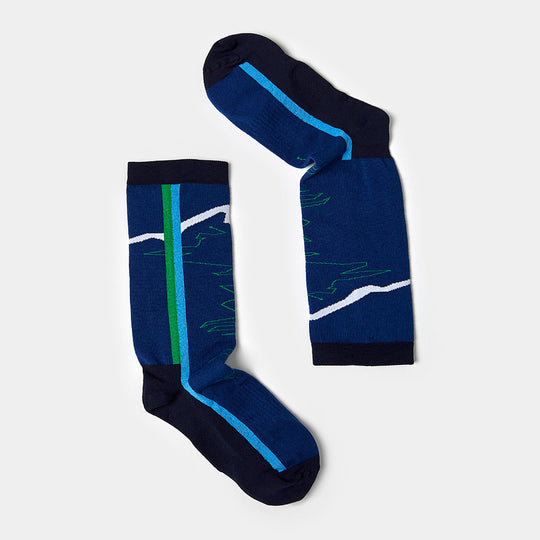 A pair of blue crew socks featuring navy toes, heels, and cuffs, with a green stripe and a white zigzag pattern resembling a mountain range on the sides. The socks are laid flat against a light gray background.